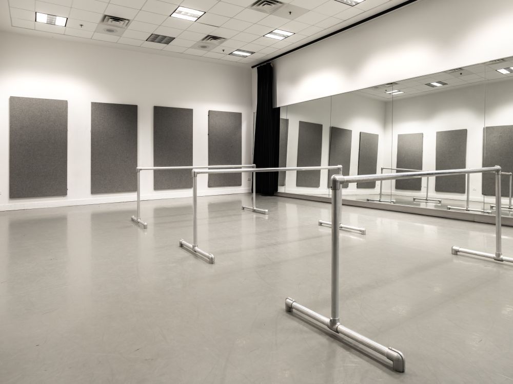 Image of an empty rehearsal room filled with wall mirrors and three bars for dancers. 