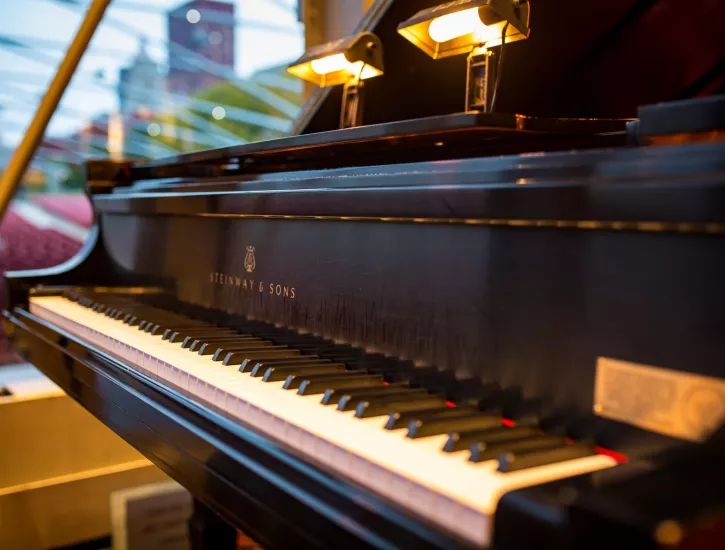 Close-up image of a black grand piano, with an outdoor pavilion and Chicago skyline in the background