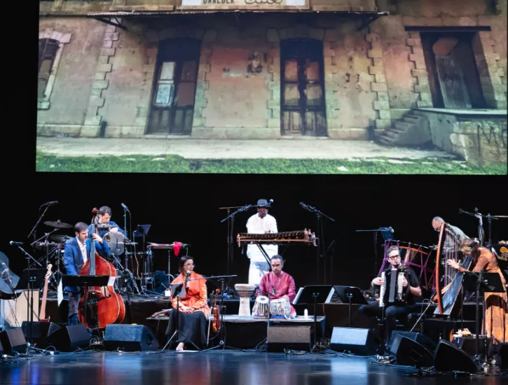 Silkroad Ensemble on the Harris stage with several instruments and a screen in the foreground projecting a building.