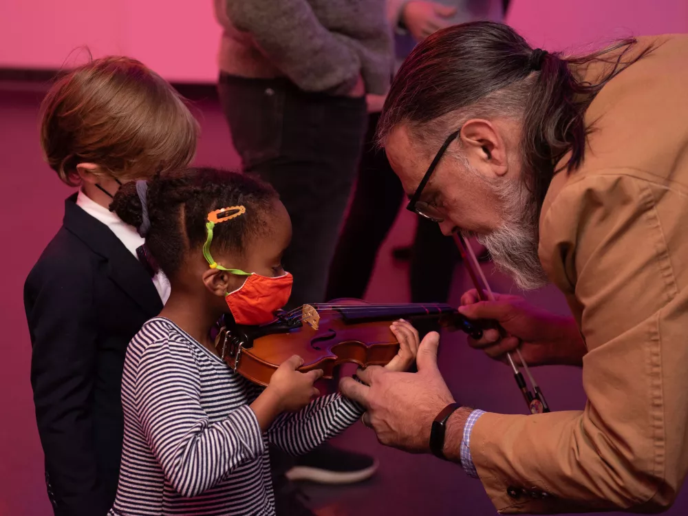 Two young children learning about instruments at the instrument petting zoo by Merit School of Music instructor.