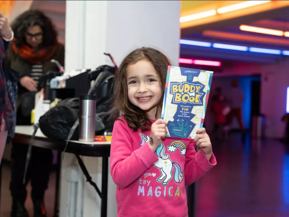 A young girl smiles while holding an coloring/activity book. 