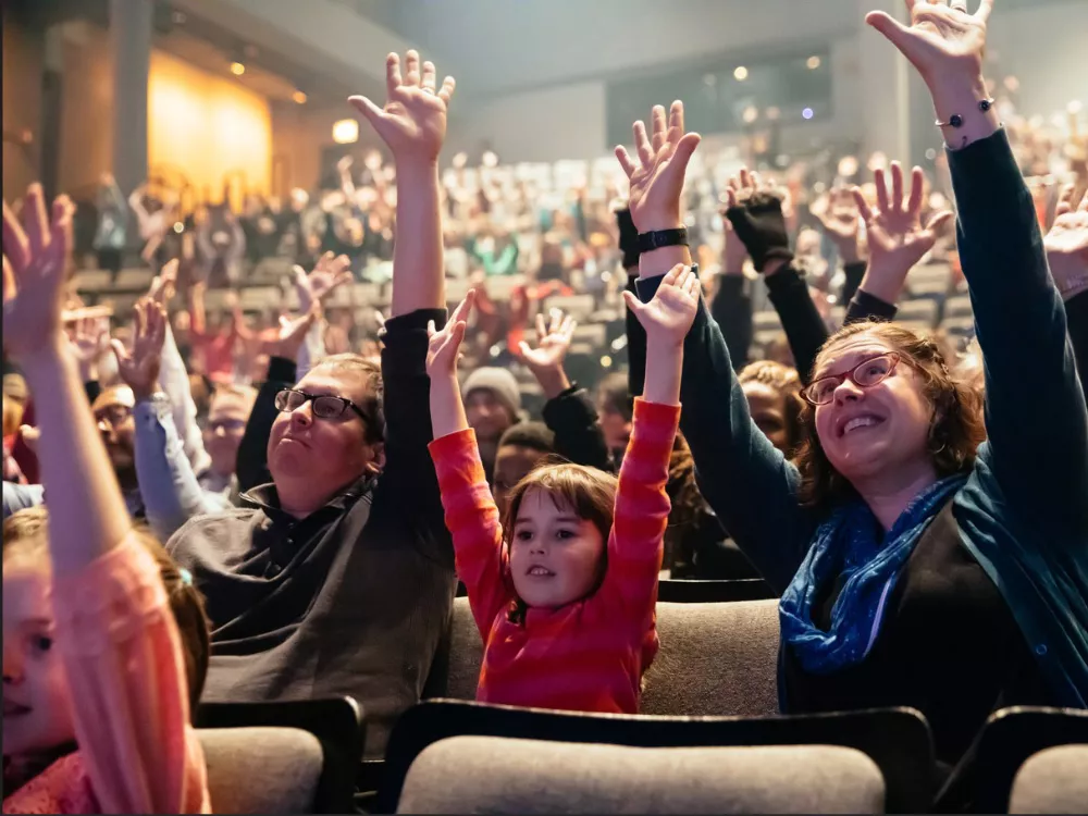 Children and their parents smile and raise their hands. 