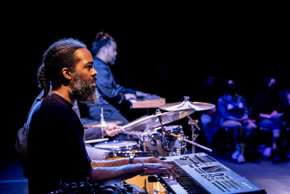 A man on stage looks out onto the audience while playing the keyboard.