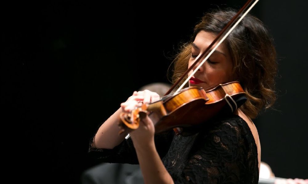 A brown-haired woman dressed in black plays the violin. 