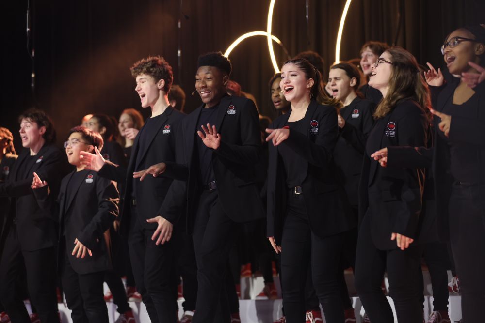 A group Voice of Chicago singing with hands up gesturing like jazz singers wearing black suits.