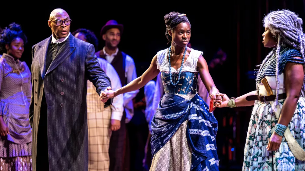 Three performers grab each others hand looking concerned at one another.