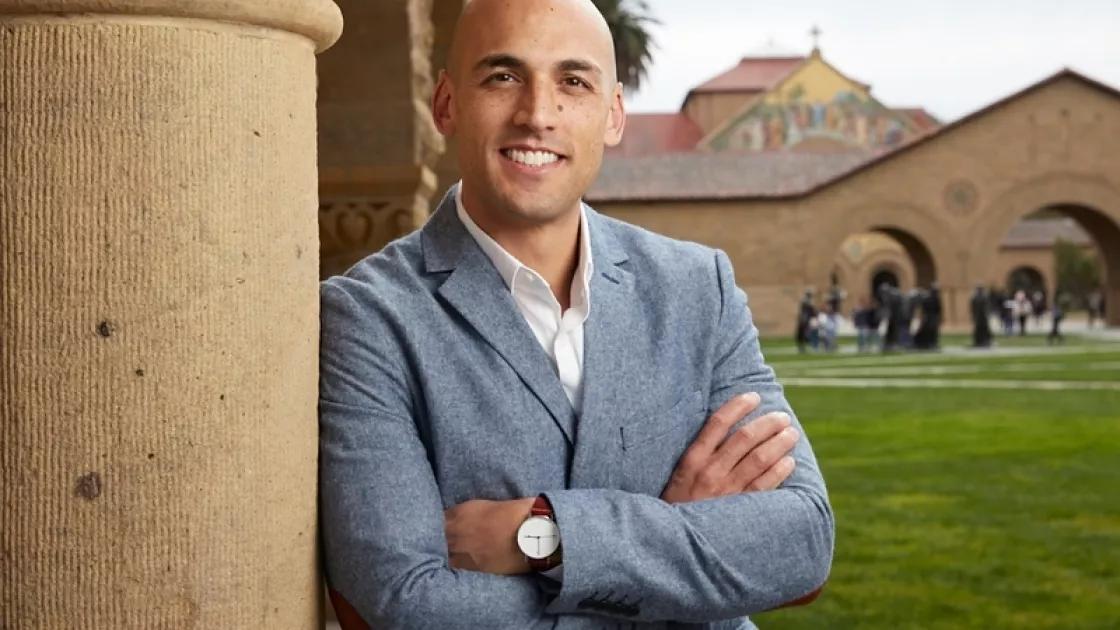 Head shot of Forrest Stuart. He is smiling with arms crossed over chest, wearing a blue suit and is leaning against a pillar.  