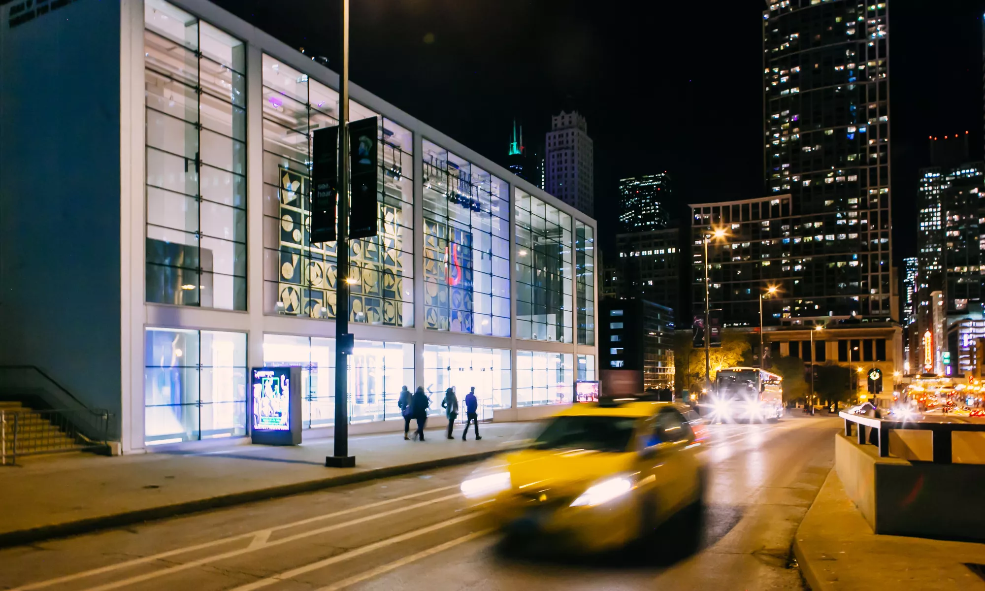 The street in front of the Harris Theater facade with a taxi rushing by