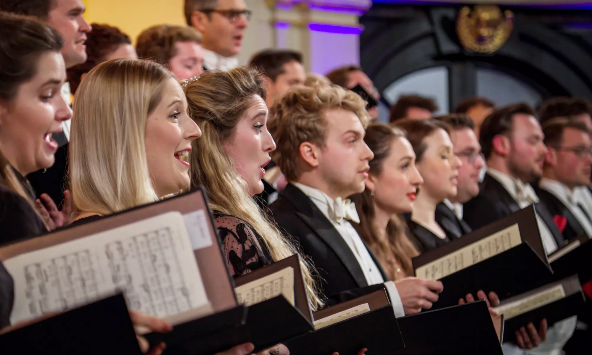 A close up of several singers holding their music folder with their sheet music.