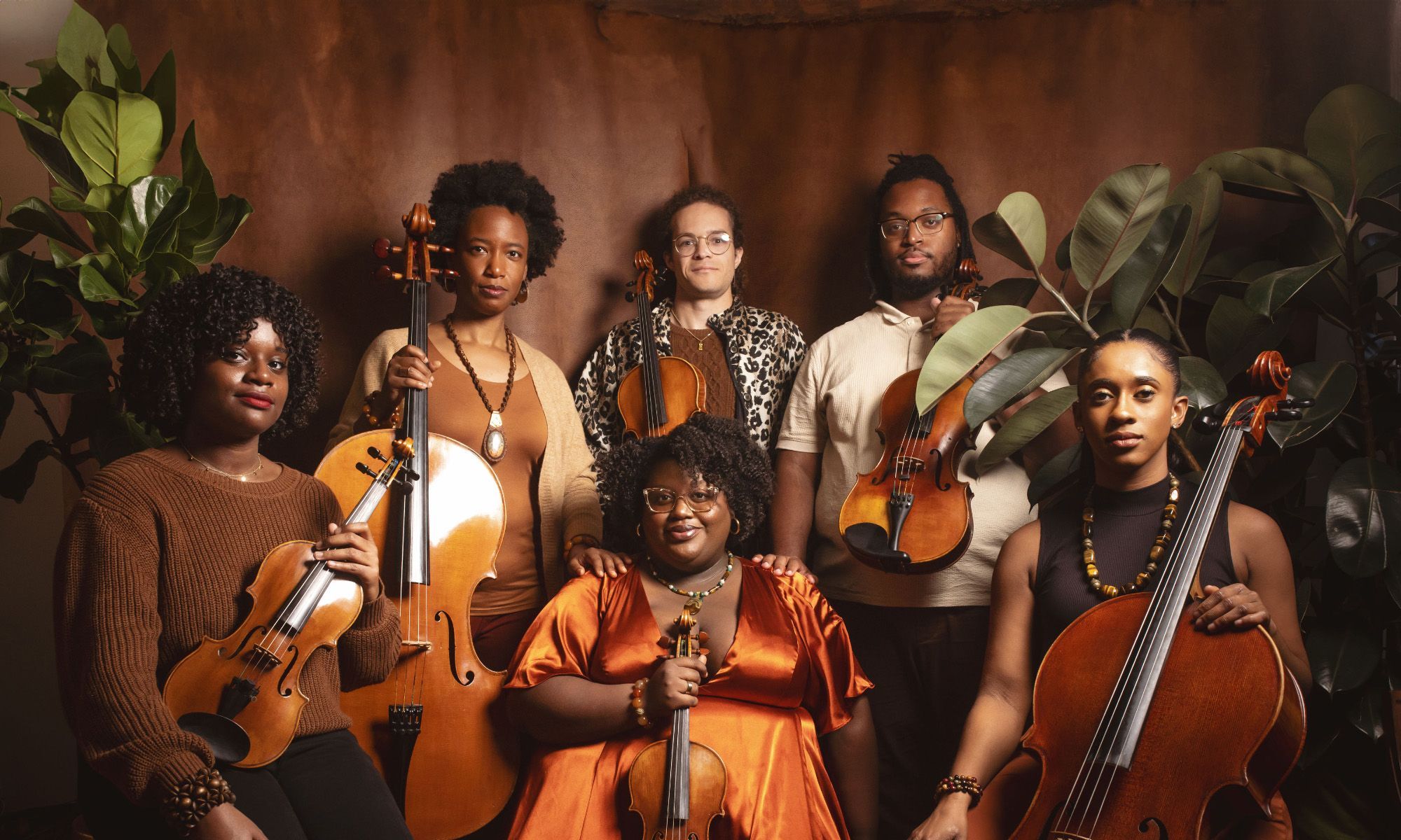 D-Composed members pose together with their instruments in front of a brown solid backdrop and plants.