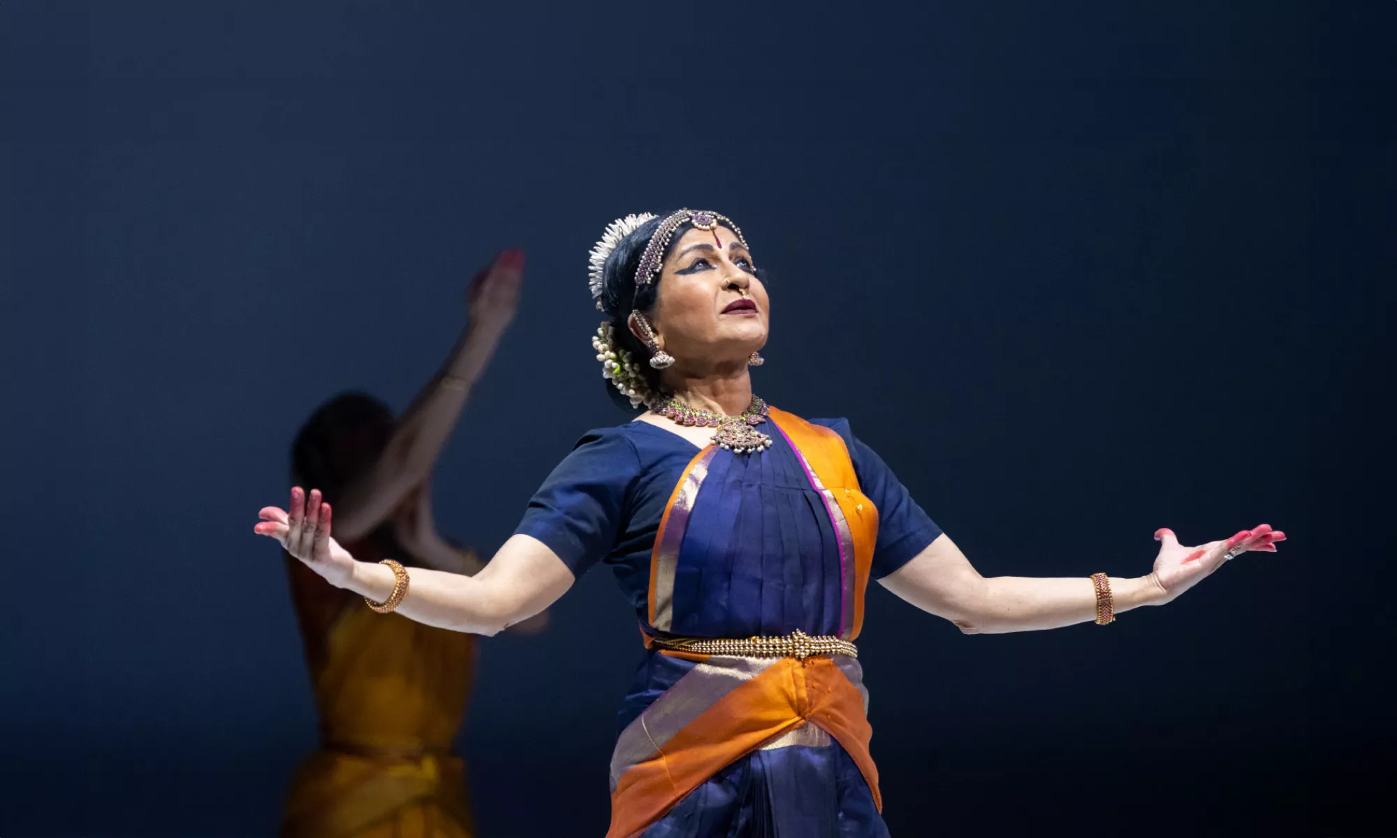 Image of a performer with her arms stretched out (palms facing up) and looking towards the ceiling.