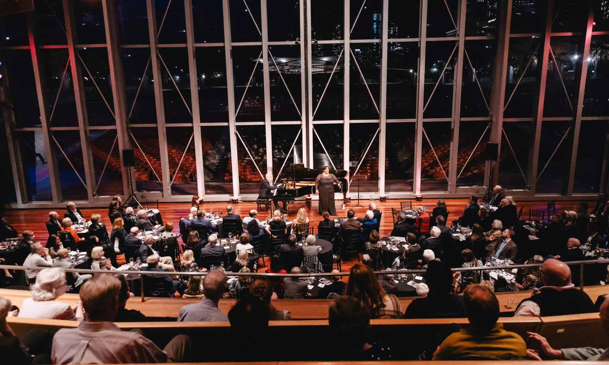 Image of an audience watching an opera singer on the Pritzker Pavilion stage amongst the night view of the Chicago skyline.