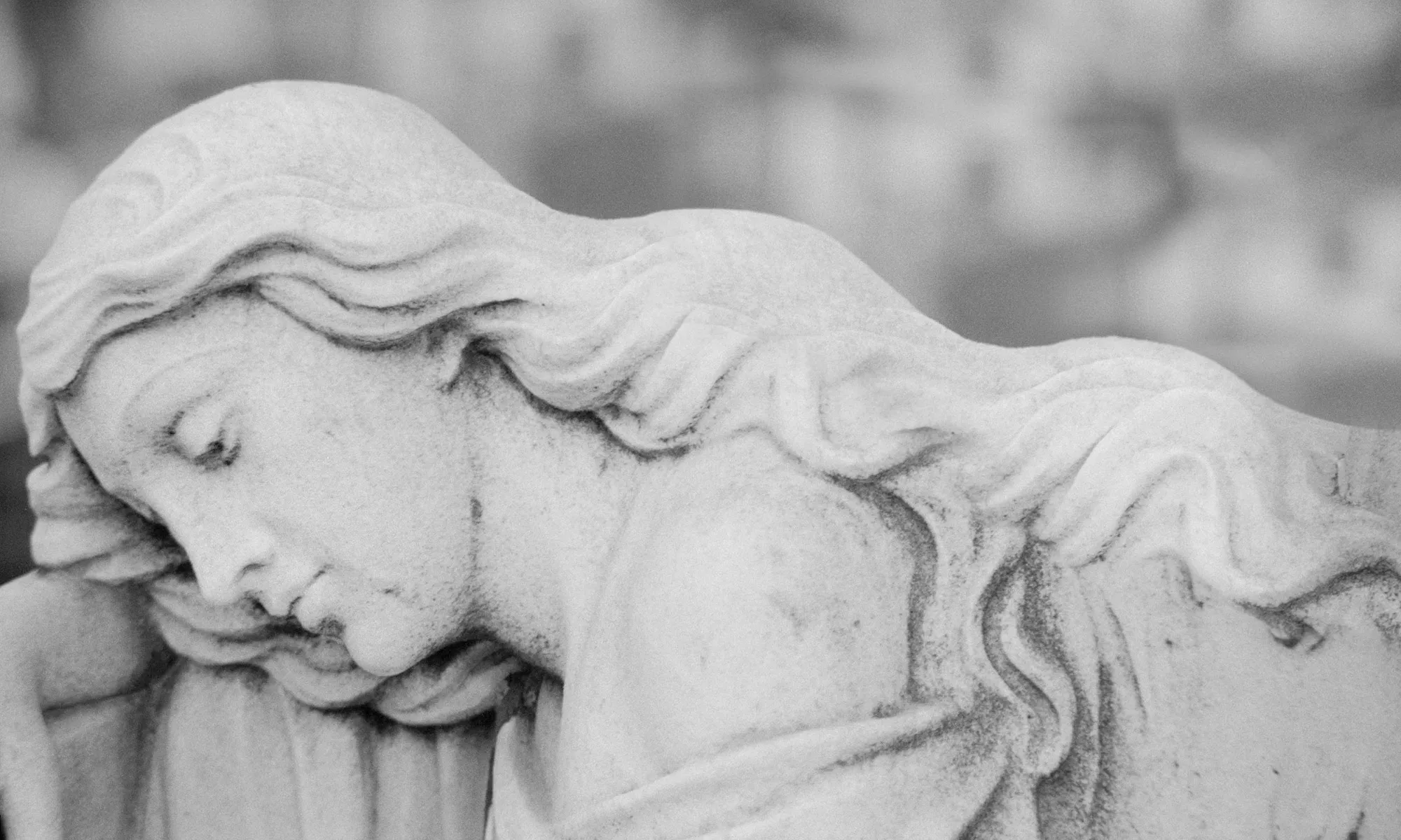 A stone sculpture of an angel resting her head.