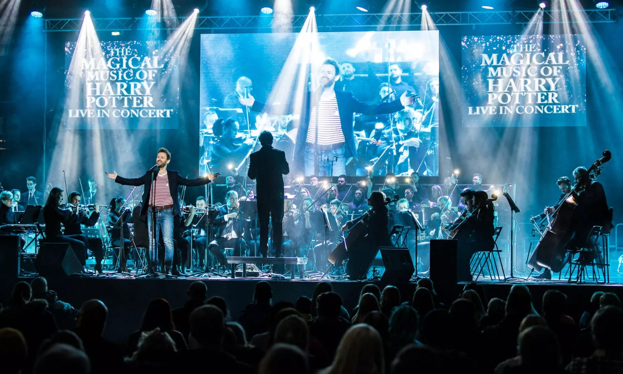 A singer at the forefront of the stage accompanied by an orchestra.