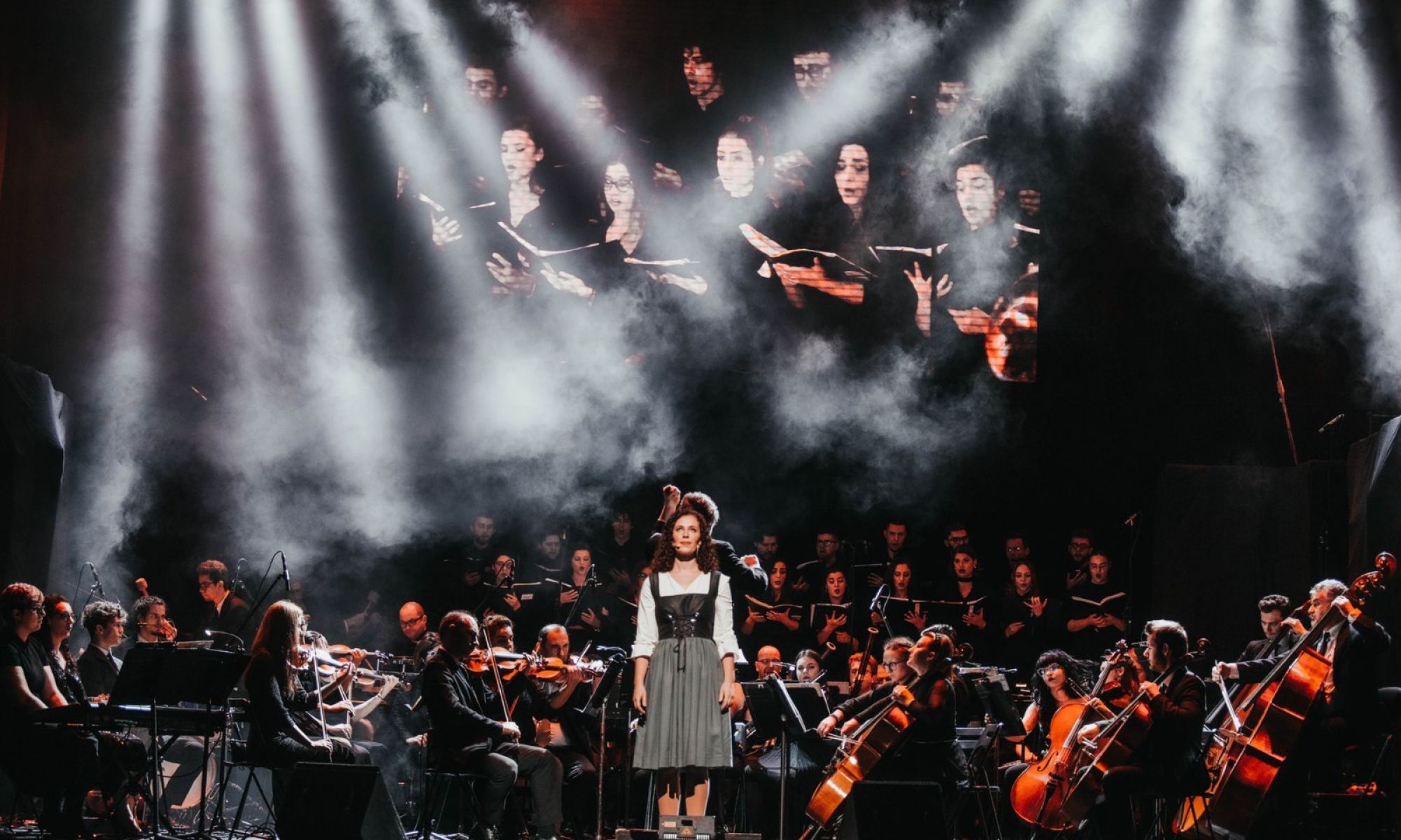 A singer at the forefront of the stage accompanied by an orchestra.