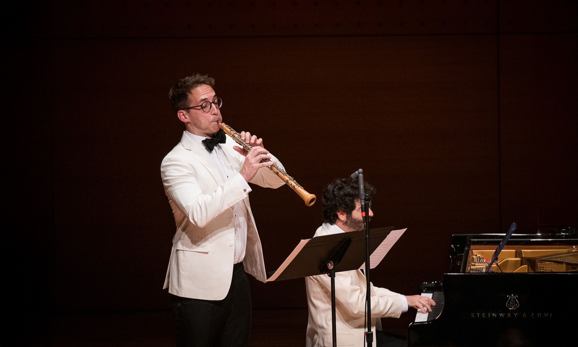 A man playing a wind instrument with his sheet music and stand. He is accompanied by a pianist.