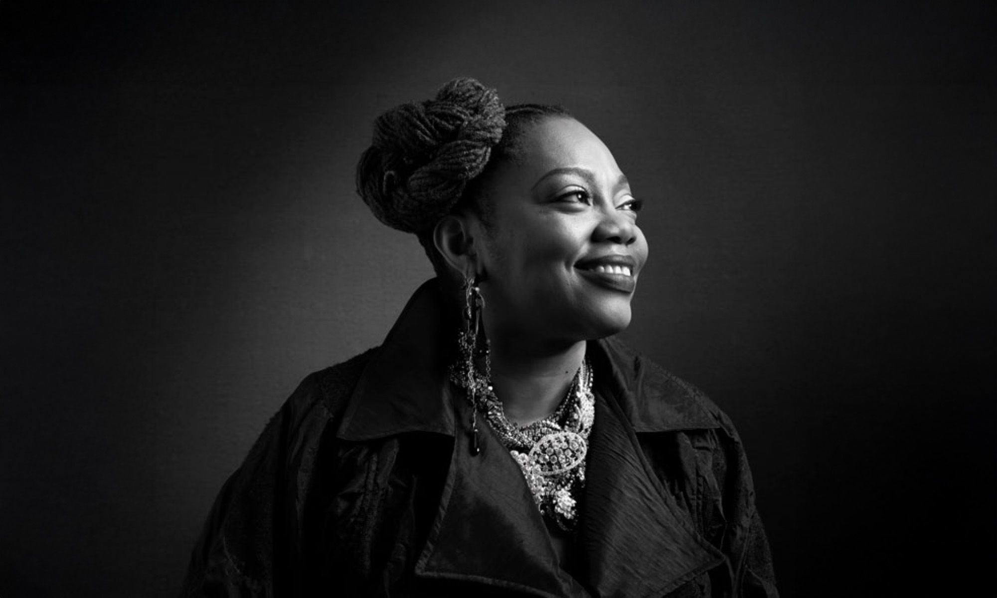 Black and white image of Dee Alexander smiling and looking to her left.