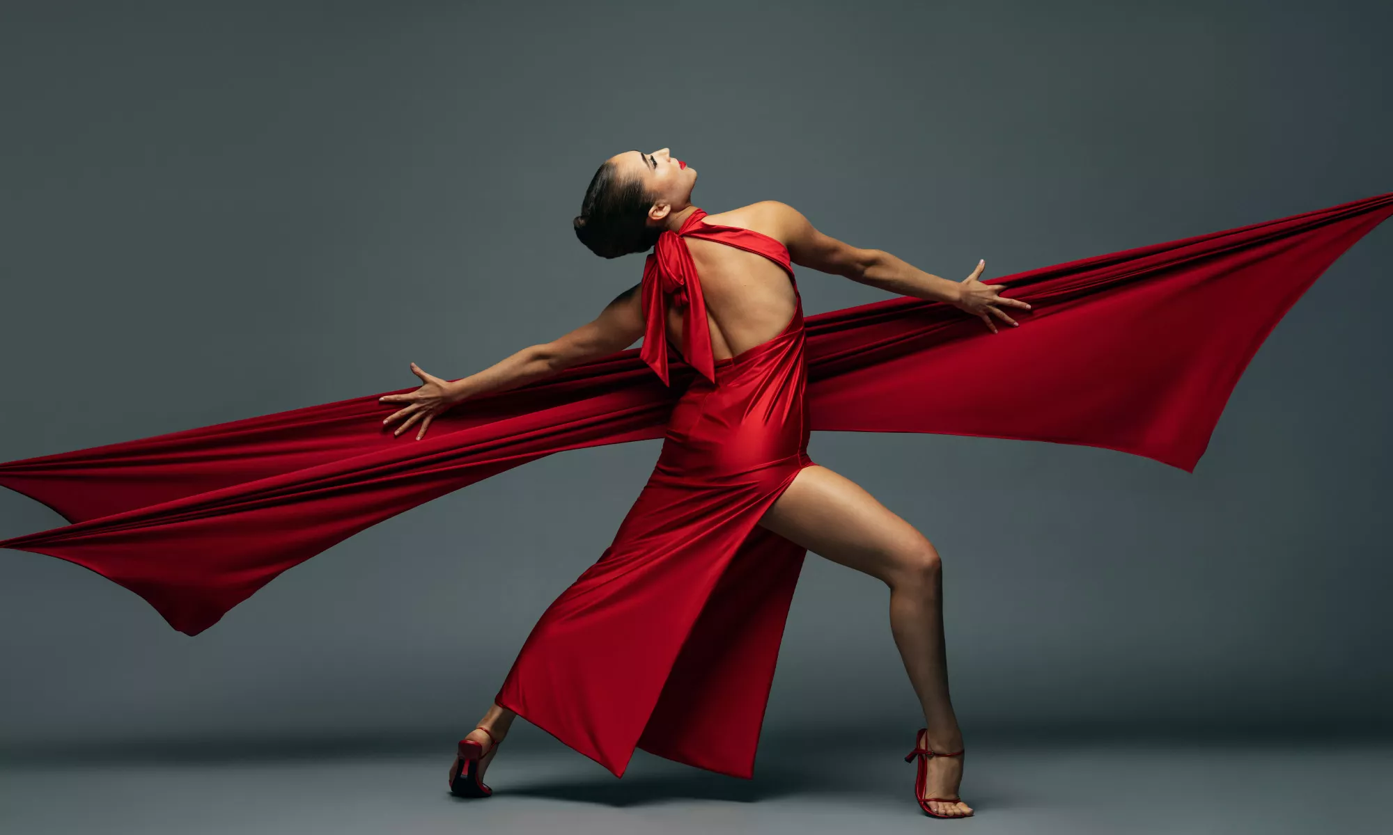 A woman in a red silk dress and heels. Her back is exposed. A red ribbon is outreached.