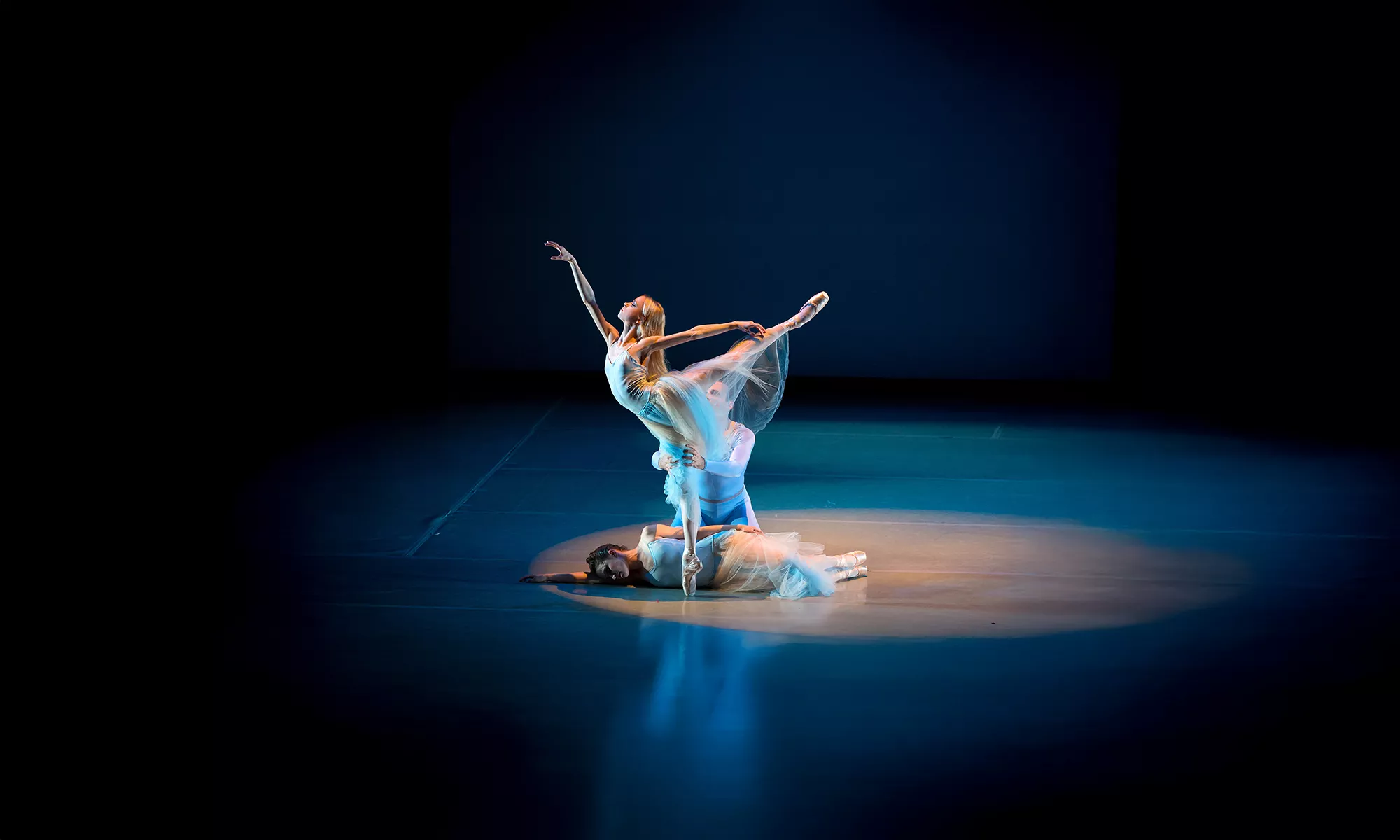 Three dancers together, one performing a high arabesque with assistance from her partner.