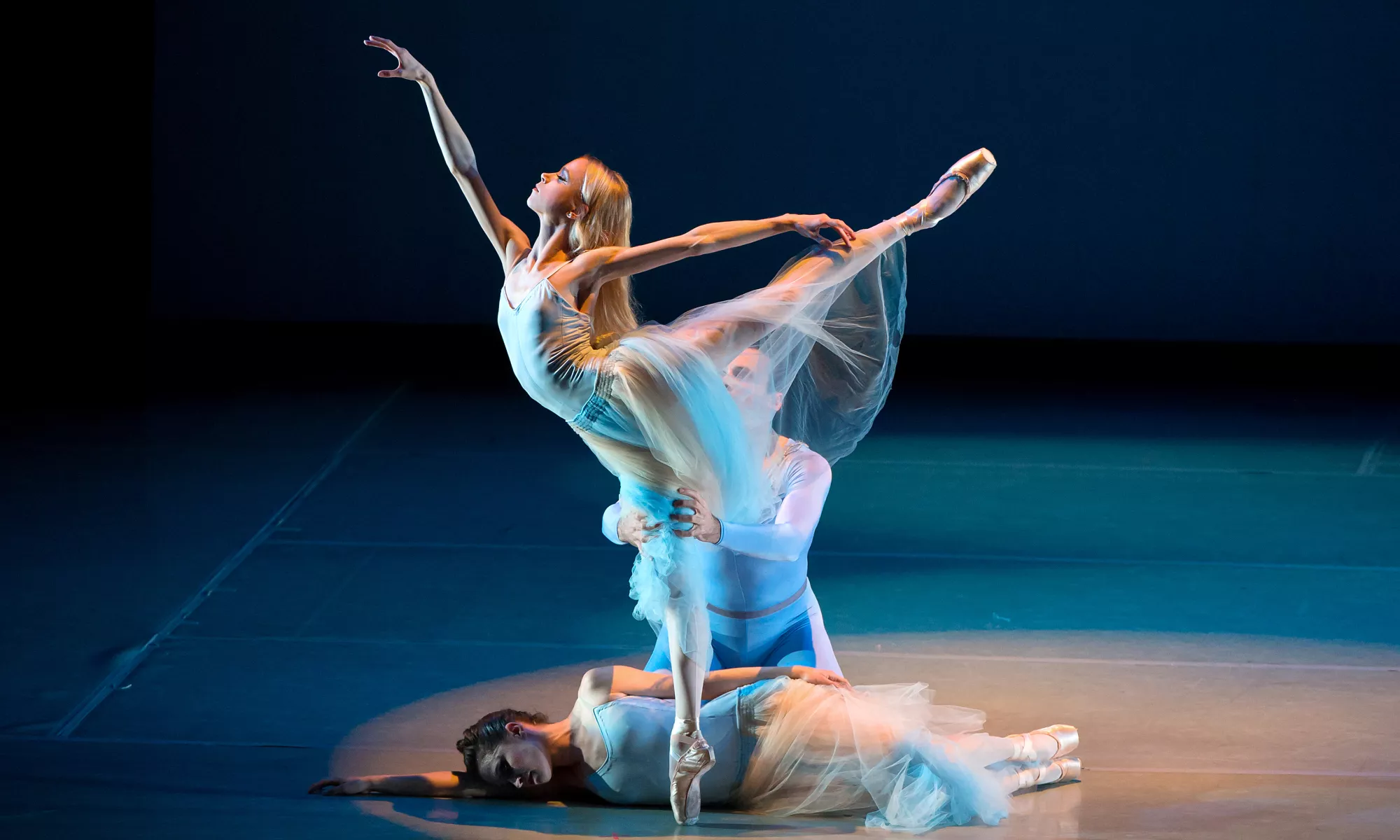 A ballerina dancing while another lays on the floor. 