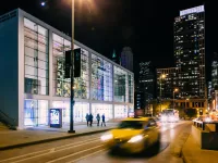 The Harris Theater at night with a yellow taxi driving by