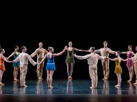 A group of dancers on stage in a circle holding hands.