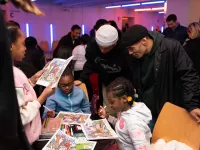 Children and adults gather around a table where the children are coloring.