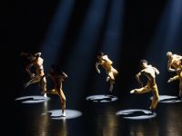 A group of dancers on stage jumping each with a spotlight.