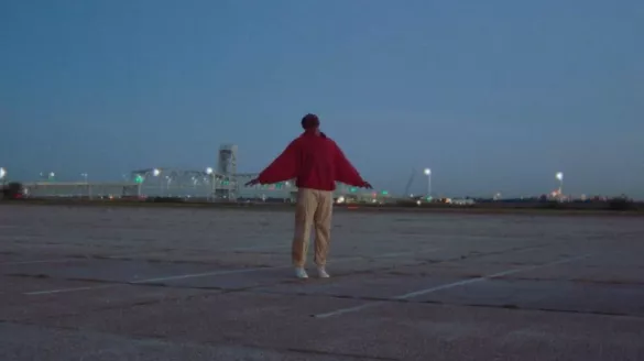 Dancer wears a red sweater and khaki pants holding their arms out