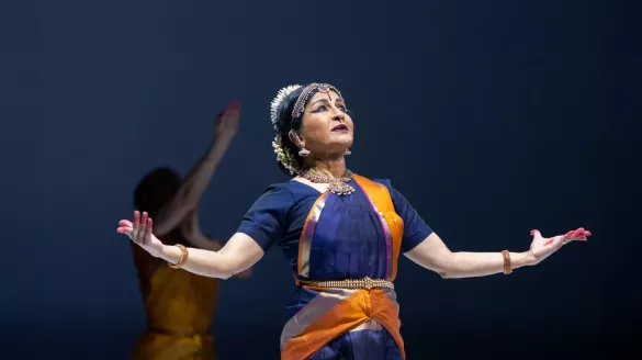 Image of a performer with her arms stretched out (palms facing up) and looking towards the ceiling.