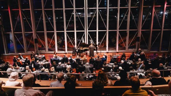 Image of an audience watching an opera singer on the Pritzker Pavilion stage amongst the night view of the Chicago skyline.