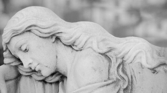 A stone sculpture of an angel resting her head.