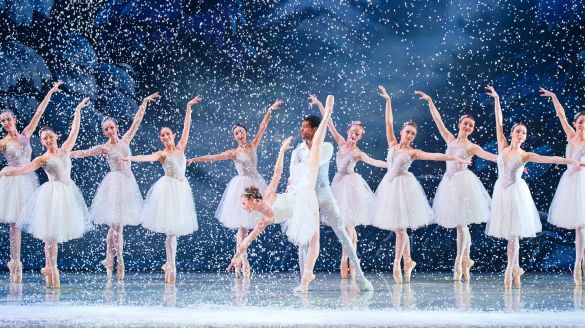 A vibrant scene from the Ballet Chicao's Nutcracker, showcasing dancers in elegant costumes amidst a magical winter backdrop. Snow is falling onstage as ballerinas pose on pointe. The Snow King and Queen are center stage.