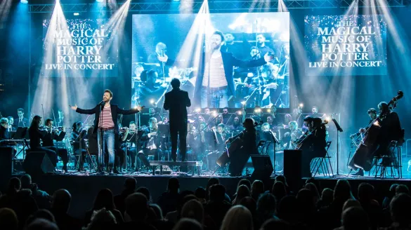 A singer at the forefront of the stage accompanied by an orchestra.