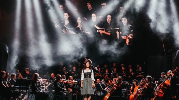 A singer at the forefront of the stage accompanied by an orchestra.