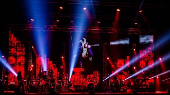 A stage with musicians shining spotlight out to the audience. A cartoon is projected on the wall.