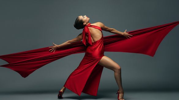 A woman in a red silk dress and heels. Her back is exposed. A red ribbon is outreached.