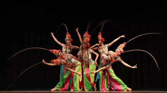 A group of dancers gather together encircling one dancer in the middle. 