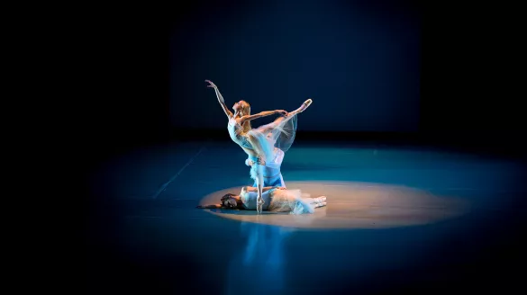 Three dancers together, one performing a high arabesque with assistance from her partner.