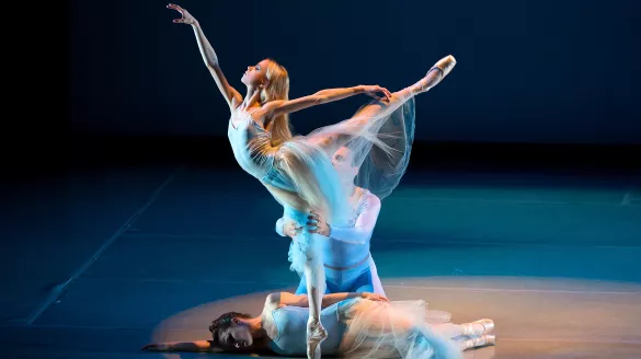 A ballerina dancing while another lays on the floor. 