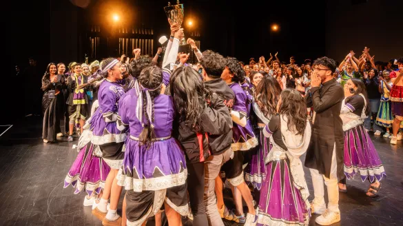 A group of people come together lifting a trophy and celebrating together.