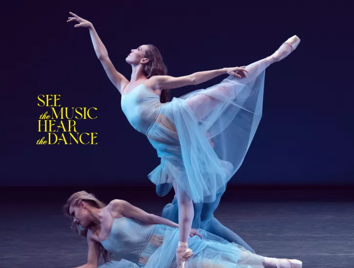 Two dancers on stage with baby blue dresses. One is lying on the floor while the other is in an arabesque position. A third dancer is hidden in the back.