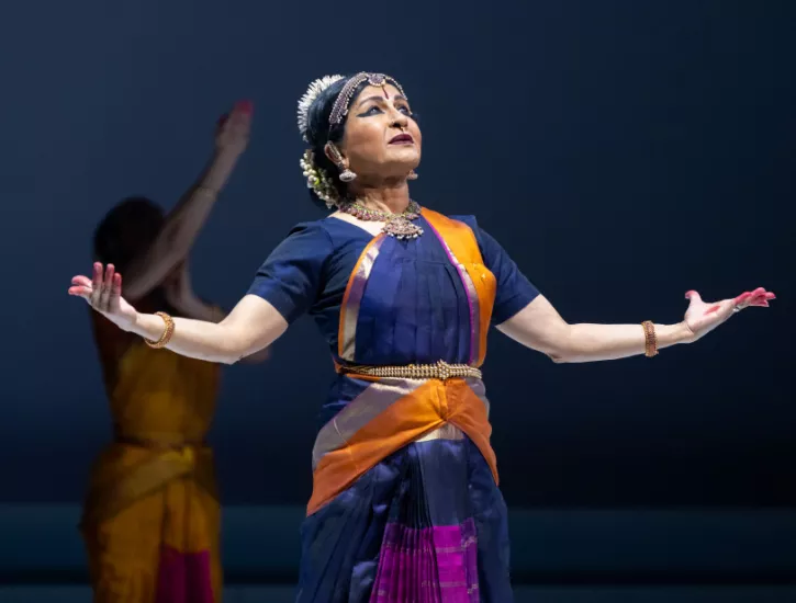 A performer on stage with her hand extended out and palms and head facing upwards.